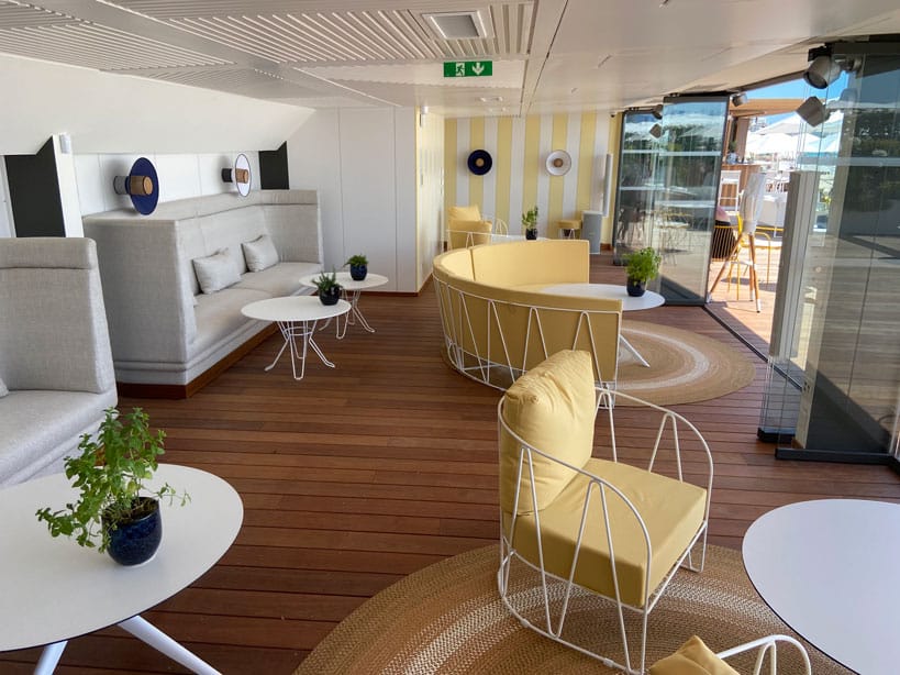 Espace intérieur élégant avec mobilier moderne, canapés jaunes et plantes décoratives sur sol en bois, lumière naturelle filtrant à travers grandes fenêtres vitrées.