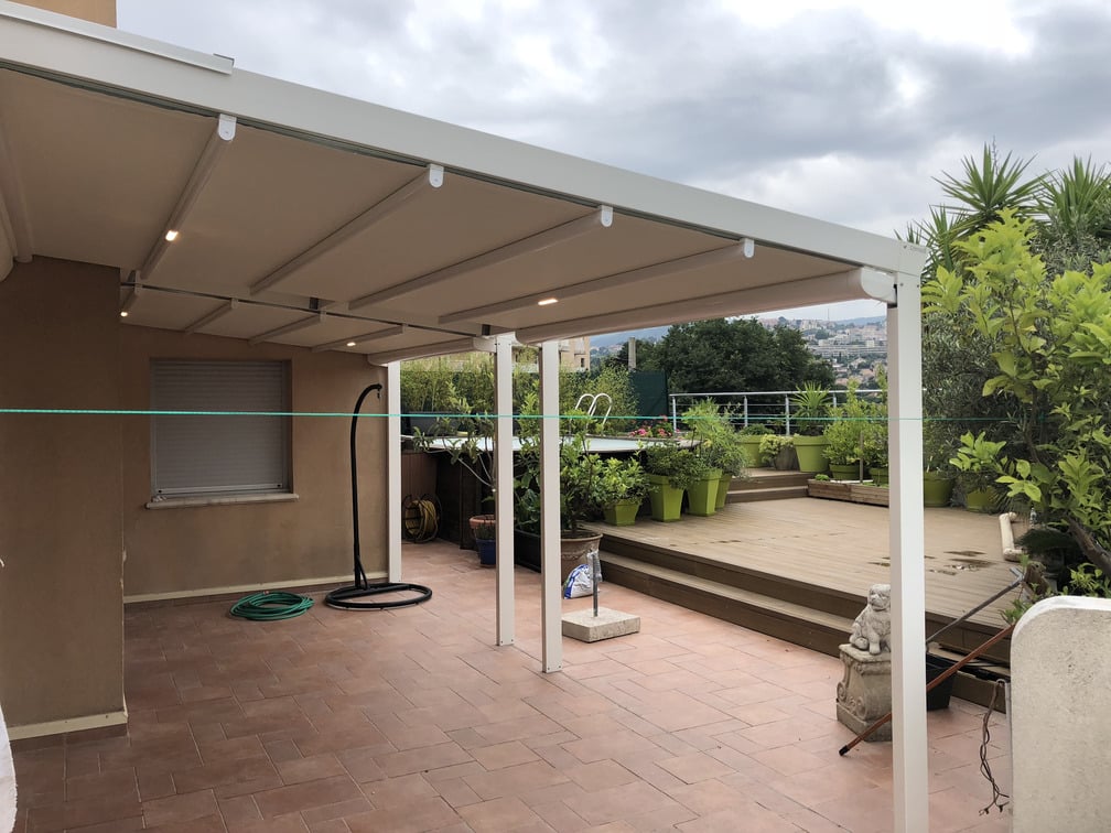 Terrasse avec pergotenda Corradi moderne, jardinières alignées et ciel nuageux. Un espace extérieur décoré de plantes vertes, sans personnes ni bâtiments reconnaissables.